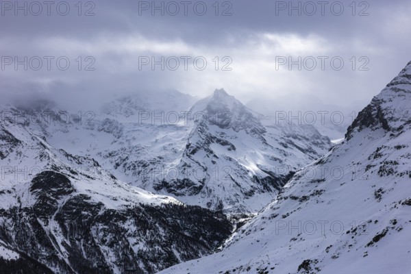 Dark clouds and wafts of mist surround the snow-covered summit of Mount Le Besso, view from the Sorebois summit station, Val d'Anniviers, Valais Alps, Canton Valais, Switzerland, Europe