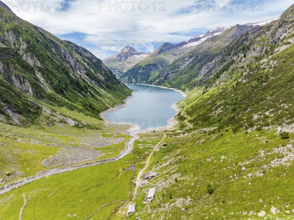 A mountain lake embedded in an alpine landscape with green meadows, mountains, a river and a hiking trail under a cloudy sky, Klein Tibet, Zillertal, Austria, Europe