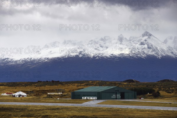 View from the deck of the cruise ship to an industrial hall in front of a snow-covered mountain range under a cloudy sky, Ushuaia, Argentina, South America