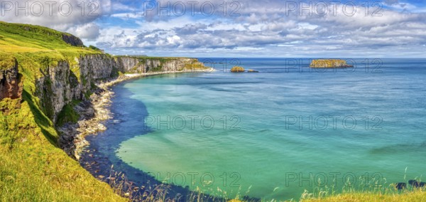 Vast coastal landscape with cliffs and bright blue sea under partly cloudy skies, County Antrim Coast