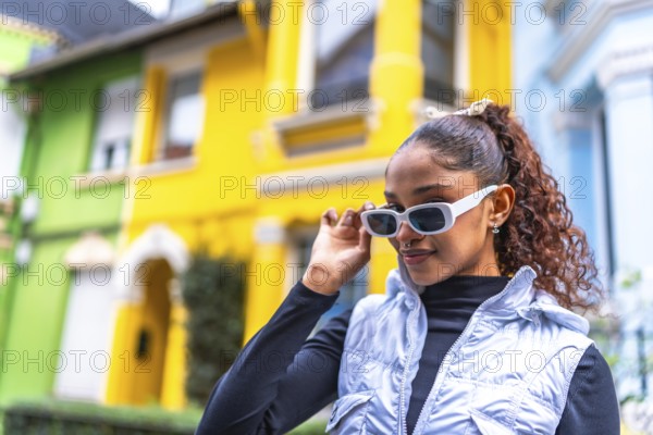 African american woman wearing modern futuristic clothes and sunglasses standing in a colorful street