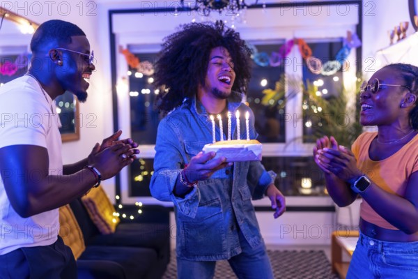 Multi-ethnic friends celebrating birthday party with cake at home at night