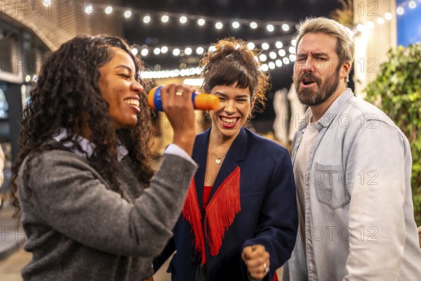 Latin woman singing karaoke next to friends at night party in the terrace of a bar