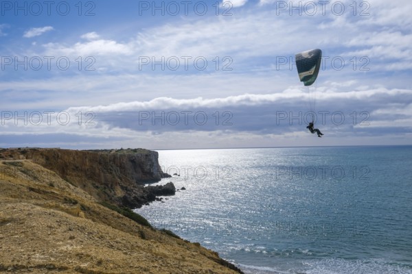 Sagres, Algarve, Portugal - Paraglider flying on the town beach Praia da Mareta, at the back left the viewpoint Ponta da Atalaia