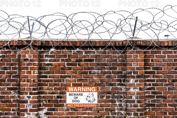 Company premises, wall secured with rolls of barbed wire, signpost for guard dog on the premises