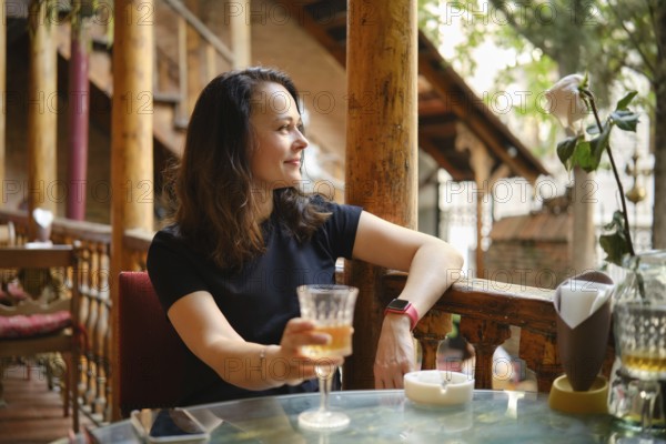 Cheerful and relaxed woman drinking white wine at rustic outdoor cafe enjoying tranquil ambiance of cozy cafe