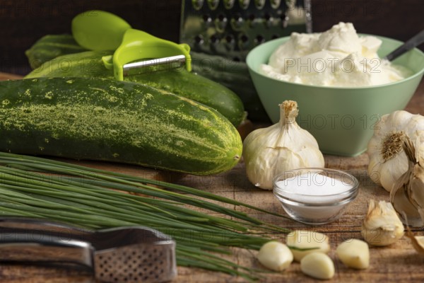 Fresh ingredients such as cucumbers, garlic, chives and sour cream on a wooden table with kitchen utensils