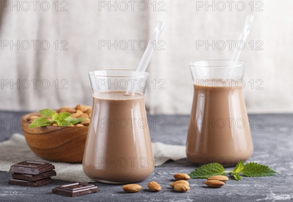 Organic non dairy almond chocolate milk in glass and wooden plate with almond nuts on a black concrete background. Vegan healthy food concept, close up, side view