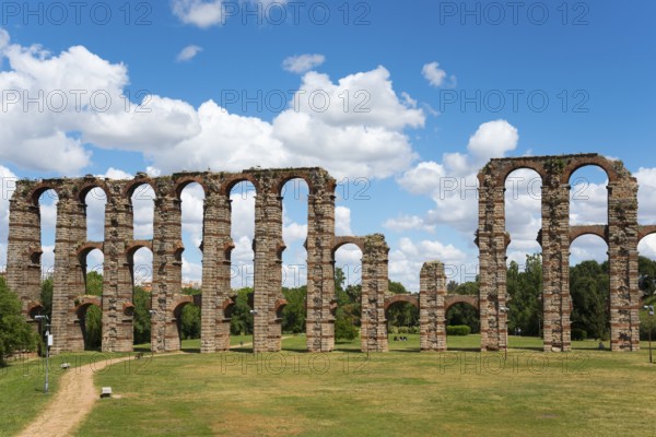 Antike Aquädukt-Ruinen mit hohen Bögen vor einem klaren Himmel und einer weitläufigen Grünfläche, Acueducto de los Milagros, Mérida, Merida, Badajoz, Extremadura, Spanien
