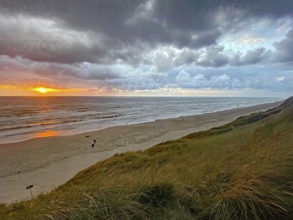 Sunset over the sea under a dramatic, cloudy sky, with people on the beach and grass dunes, holiday, Lokken, Jutland, Denmark, Europe