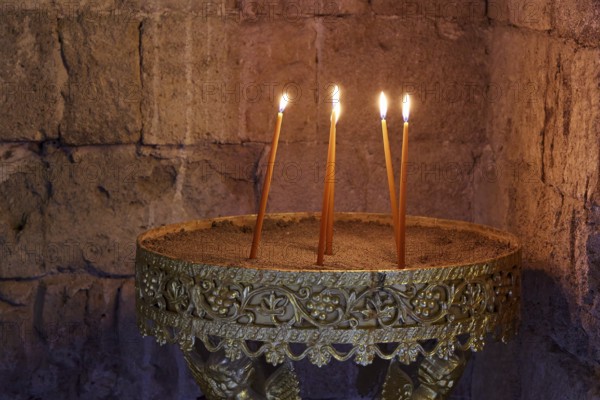 Several burning candles in an antique golden candlestick in front of a stone wall, creating a calm and warm atmosphere, Monastery of Our Lady of Mount Filerimos, Filerimos, hill not far from Rhodes Town, Ancient State of Ialyssos, Rhodes, Dodecanese, Greek Islands, Greece, Europe