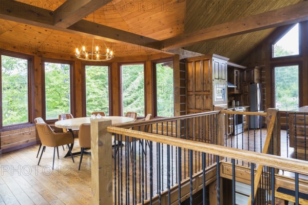 Staircase, round wooden dining table with tan leather armchairs in dining room, plus kitchen inside a milled Eastern white pine timber and flat log profile home, Quebec, Canada, North America