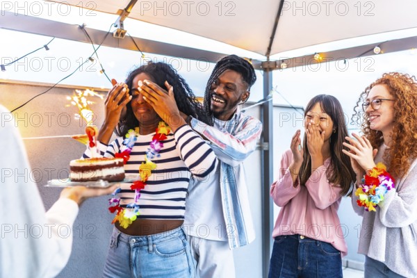 African young woman with eyes covered receiving a birthday cake from multi-ethnic friends at terrace