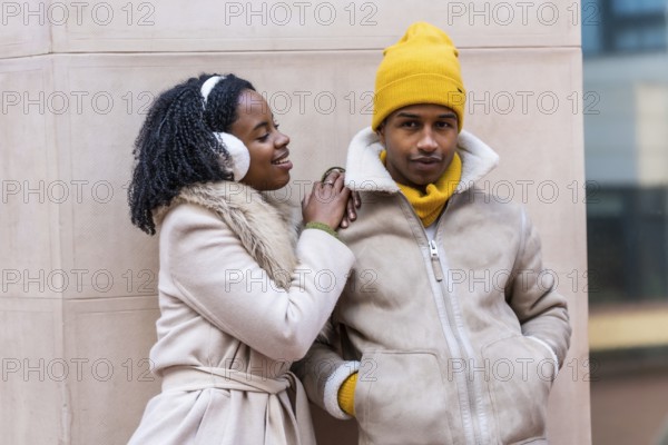 Happy couple dressed in stylish winter clothing, smiling and leaning against a contemporary city wall, enjoying their time together