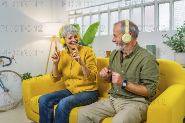 Happy senior couple listening to music and dancing sitting together on the sofa