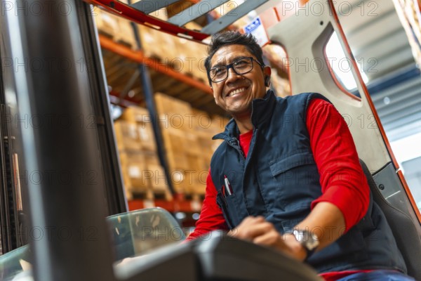 Happy latin worker smiling at camera while using forklift in a distribution warehouse