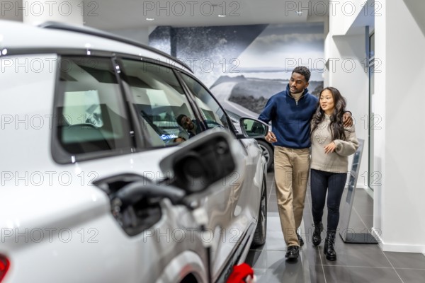 Multiethnic couple walking through a car dealership, happily selecting their new electric vehicle while enjoying the modern showroom experience
