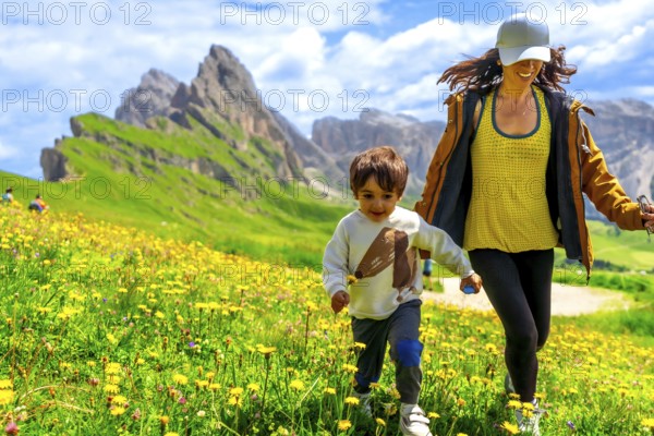 Tourists enjoying summer vacations in the italian alps, running through a field of wildflowers with the odle mountains in the background