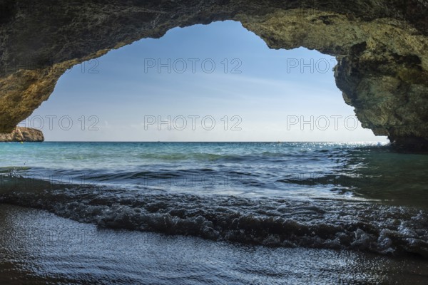 Turquoise waves gently washing onto the shore of cala domingos beach in mallorca, spain, viewed from the inside of a cave, creating a tranquil and serene scene