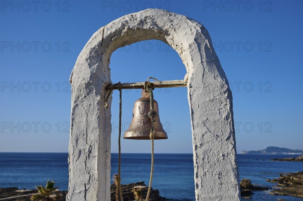 Close-up of a bell in a white frame in front of a rocky coastal landscape and blue sky, rock church Agios Nikolaos, Oasis Beach, Kallithea, Rhodes, Dodecanese, Greek Islands, Greece, Europe