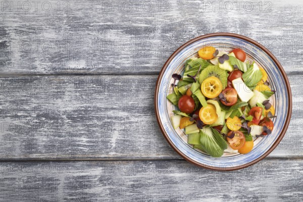 Vegetarian salad of pac choi cabbage, kiwi, tomatoes, kumquat, microgreen sprouts on gray wooden background. Top view, flat lay, copy space