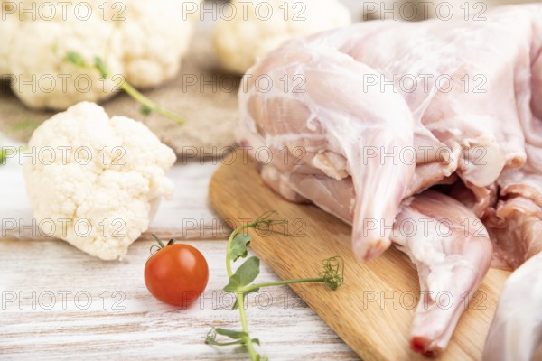 Whole raw rabbit with cauliflower, tomatoes and spices on a white wooden background and linen textile. Side view, close up, selective focus