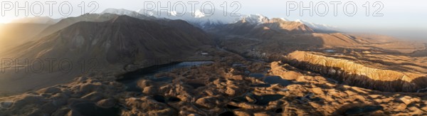Panorama, White glaciated and snow-covered mountain peak Pik Lenin at sunrise, hilly landscape with golden meadows and lakes, aerial view, Trans Alay Mountains, Pamir Mountains, Osh Province, Kyrgyzstan, Asia