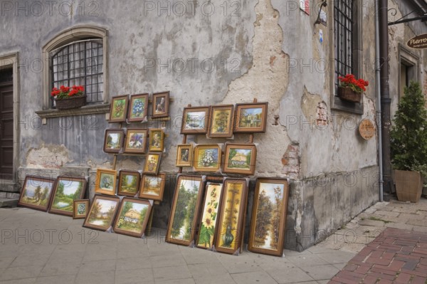 Framed paintings displayed against an old damaged grey cement wall in the Old Town Market Square, Warsaw, Poland, Europe