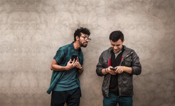 Young man spying on his friend's cell phone. Young man spying friend using phone