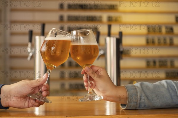 Close-up of two hands clinking glasses of craft beer in a modern bar. The atmosphere is warm and welcoming, perfect for a social gathering or daytime celebration