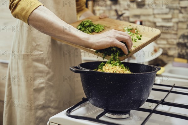 Unrecognizable man pours chopped green onions into a saucepan on a gas stove