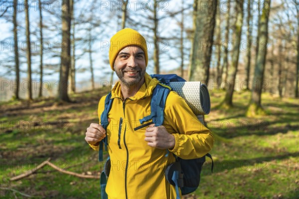 Hiker in a bright yellow jacket and backpack smiling while trekking through a sunlit forest, enjoying the beauty of nature on a perfect day