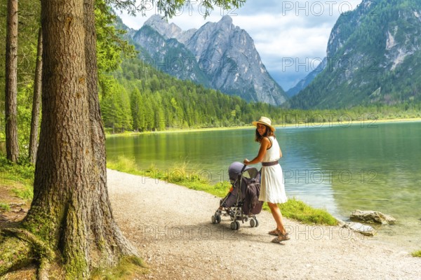 Tourist walking with stroller along lake in breathtaking mountain scenery of dolomites, italy, enjoying summer holiday