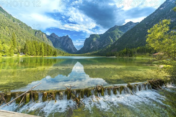 Crystal clear water flowing from lake dobbiaco, surrounded by majestic dolomites peaks, on a sunny summer day in italy