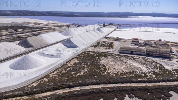 Aerial view of large salt cones forming alongside a pink lake and salt mine at sunset in torrevieja, spain