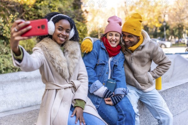 Three young multi ethnic friends are taking a selfie in a winter city, smiling and enjoying their time together