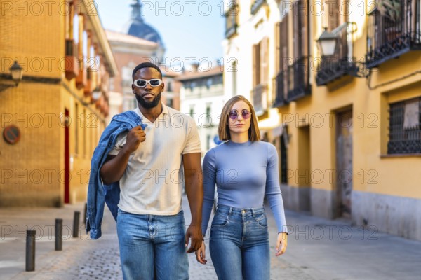 Frontal view of a stylish multiracial couple walking together with cool attitude along street