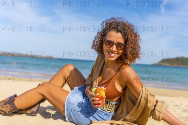 Happy sensual woman sitting on sandy beach enjoying tropical fruit sliced inside a plastic take away glass