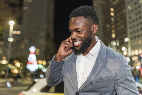 Young businessman smiling and chatting on a mobile phone while enjoying the vibrant city nightlife, surrounded by twinkling lights
