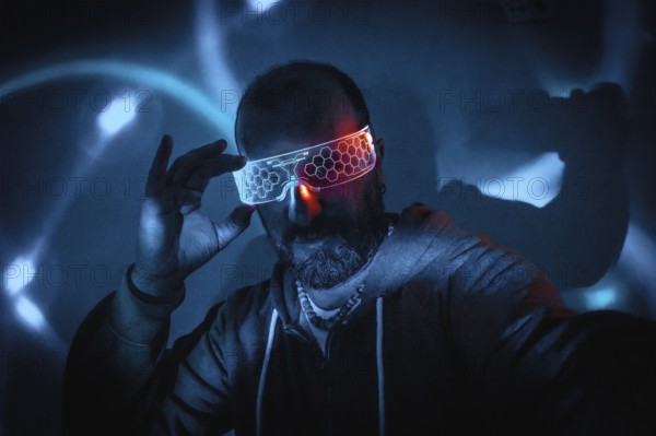Bearded man adjusting futuristic glowing smart glasses in dark cyberpunk setting with blue and turquoise neon lights