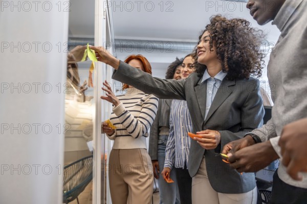 Hispanic beauty woman using adhesive note on glass during creative process in a modern coworking