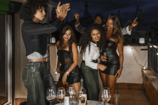Happy multiracial friends clasping and dancing during summer night party in a roof