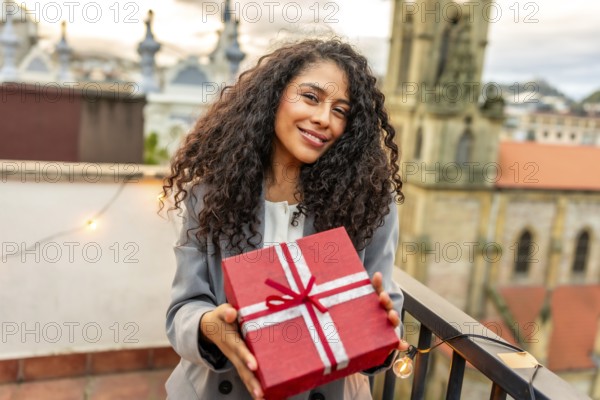 Portrait of a happy hispanic woman receiving a birthday present in a rooftop