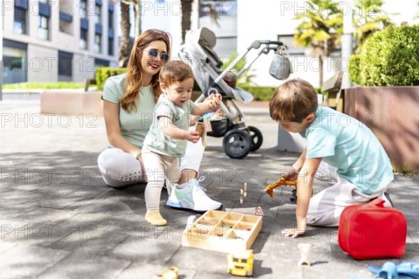 Full length photo of a happy woman and sons playing with toys in an urban space