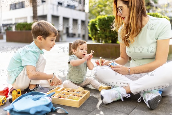 Full length photo of a young mother and children playing and learning on an urban park