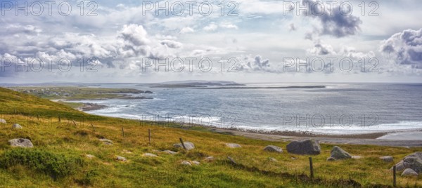 Panoramic view of a picturesque coastal landscape with cliffs, green grass and calm sea under a cloudy sky, Northern Ireland