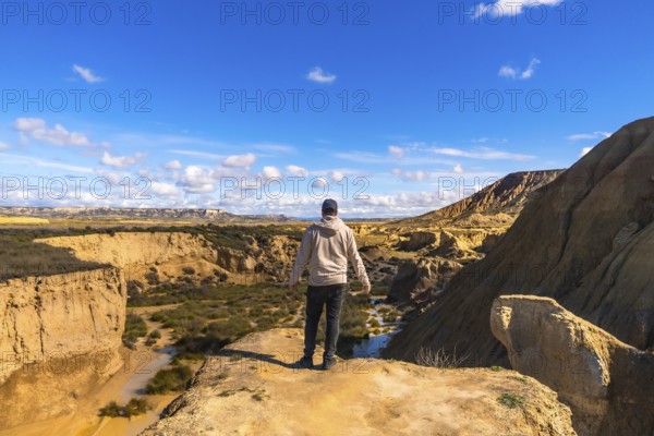 Tourist standing on cliff edge admiring the stunning landscape of bardenas reales desert in navarre, spain, a unique geological formation