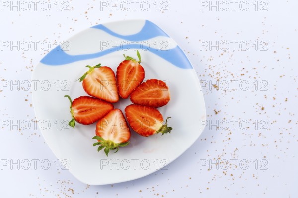 Aerial view of cut strawberries on a white plate with a white background with brown sugar