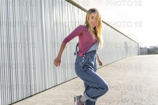 Happy blonde woman wearing casual clothes dancing a modern urban dance outdoors in the street