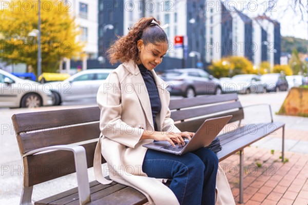 Side view photo with copy space of a beauty elegant african woman sitting on a city bench using laptop